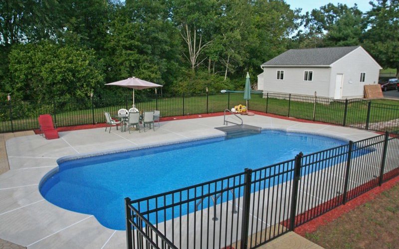 This is a photo of a roman in ground pool in Stuyvesant, NY with custom pavers, black fence and steps.