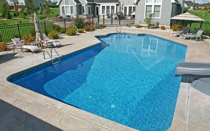 This is a photo of a Lazy L style custom inground swimming pool with a black fence, steps and water slide.