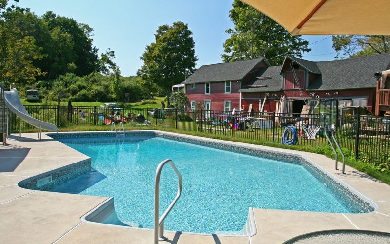 This is a photo of a Lazy L style custom inground swimming pool with a black fence, steps and water slide.