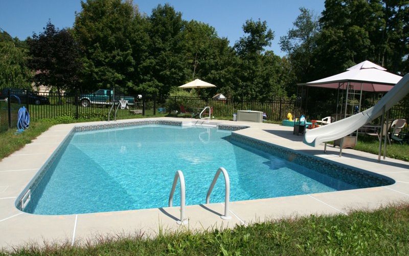 This is a photo of a Lazy L style custom inground swimming pool with a black fence, steps and water slide.